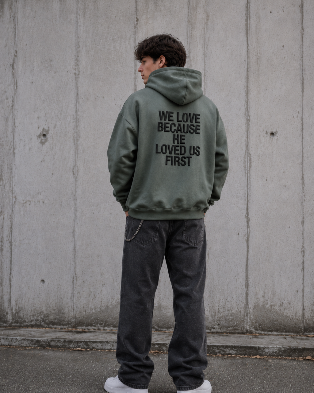 Person wearing a green hoodie with text on the back, standing against a concrete wall.