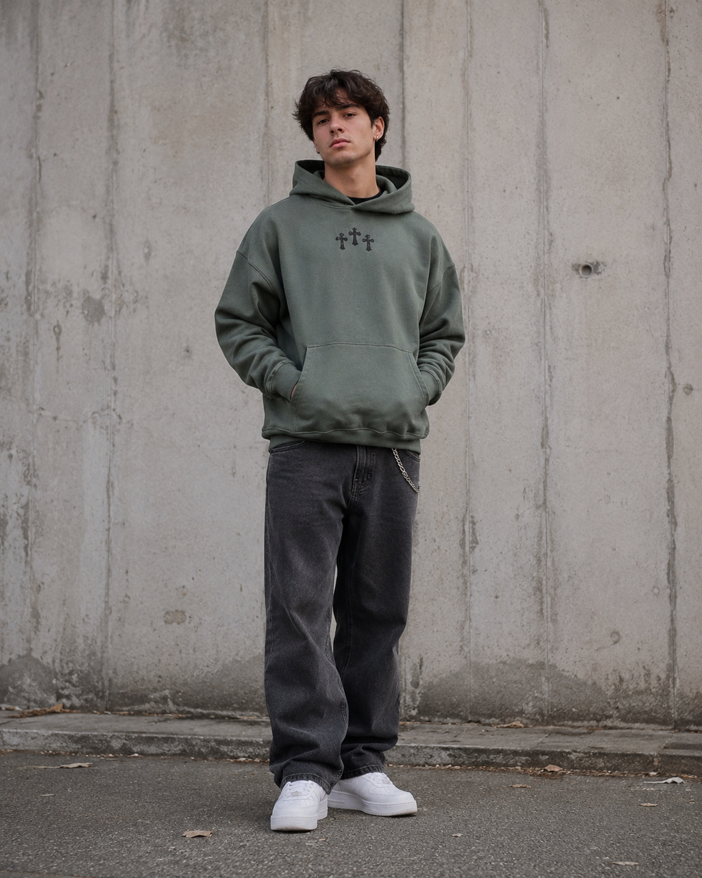 Person wearing a green hoodie with a logo against a concrete wall.