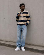 Person wearing a striped sweater and jeans standing against a concrete wall.
