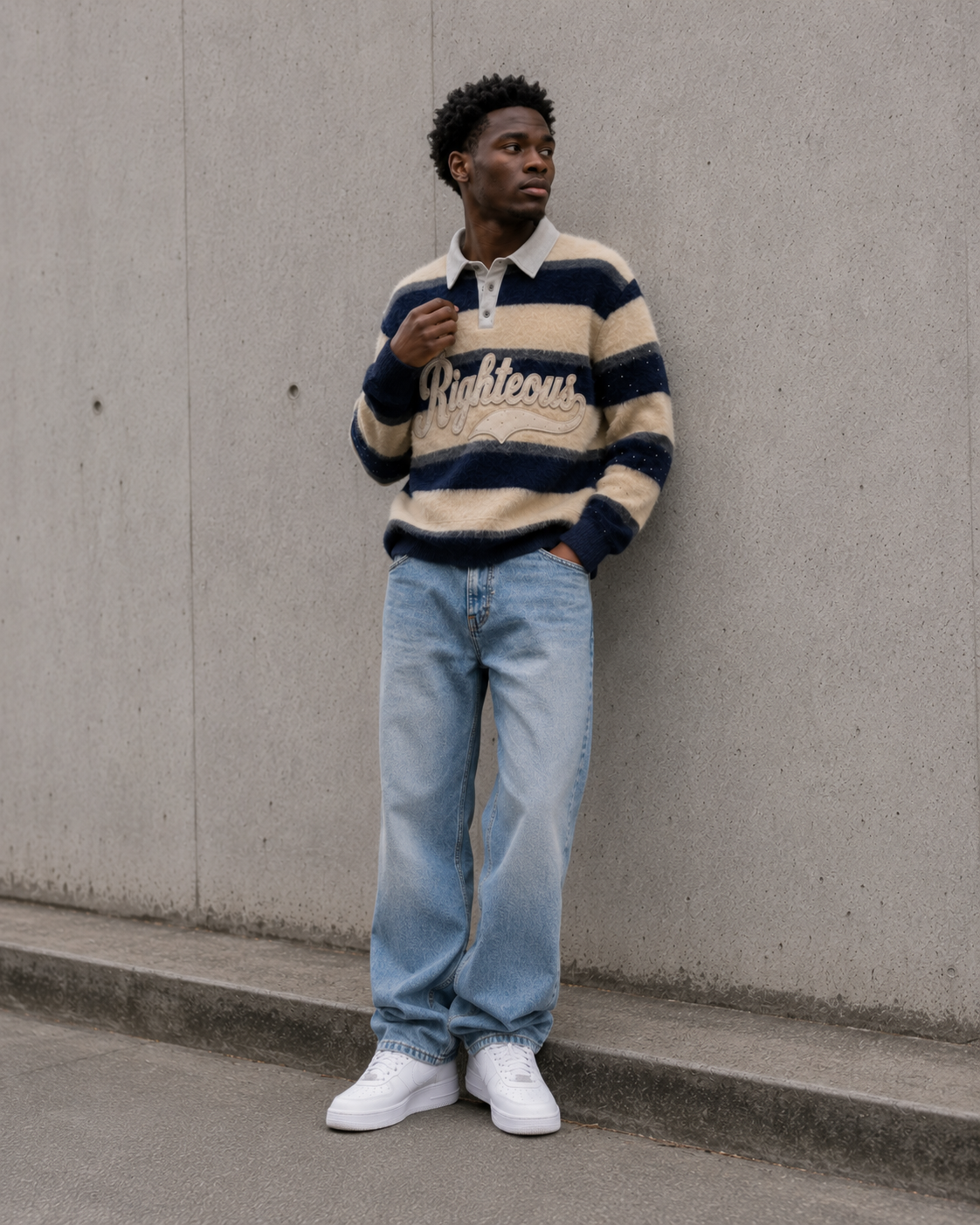 Person wearing a striped sweater and jeans standing against a concrete wall.