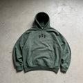 Green hoodie with black cross design on a gray concrete surface