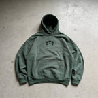 Green hoodie with black cross design on a gray concrete surface