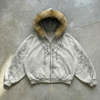 White hoodie with fur hood and intricate designs on a concrete surface