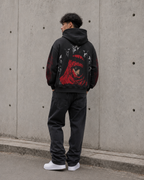 Person wearing a black hoodie with a red graphic design against a concrete wall.